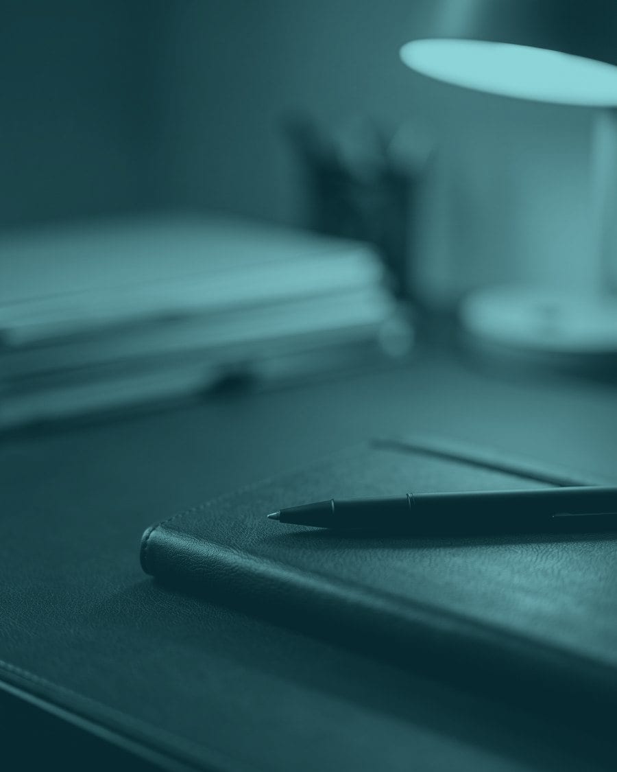 A notebook and pen on a desk under lamplight